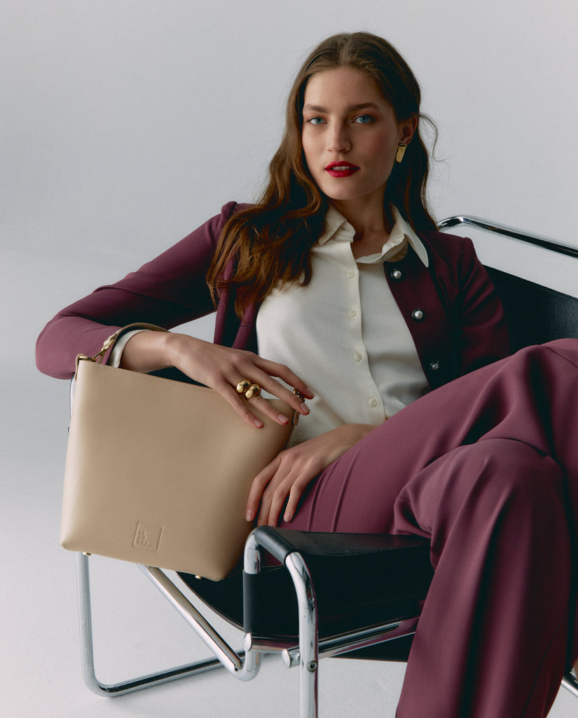 Imagen de modelo sentada con bolso tote bag. Bolso de hombro tipo tote de piel beige multiposición Leandra. Fabricado en España.