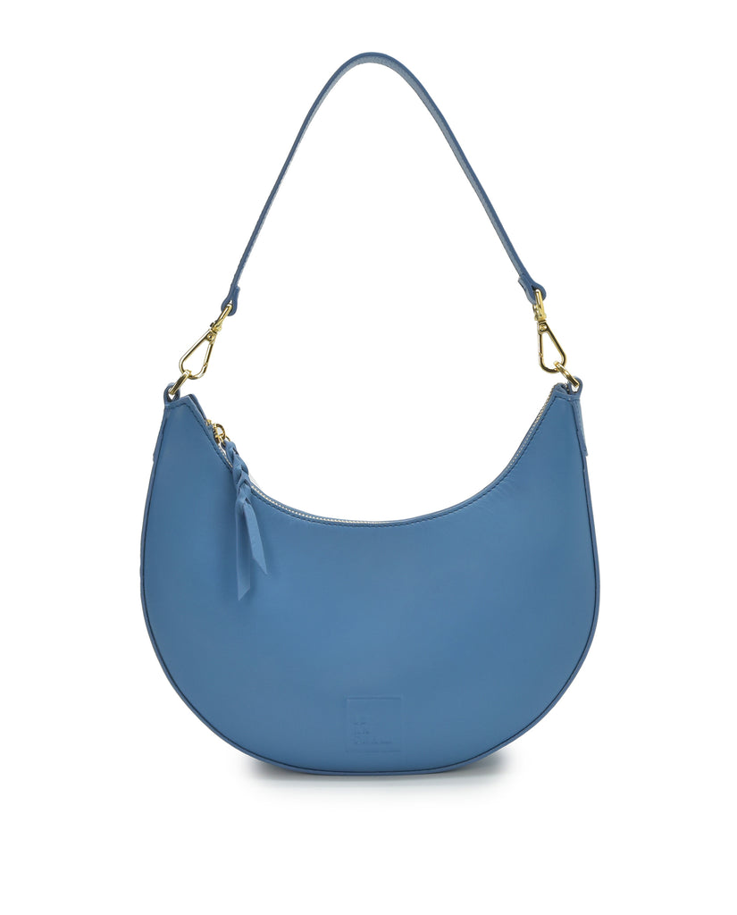 Imagen asa corta de bolso media luna azul Leandra. Bolso de hombro multiposición con forma de media luna de piel color azul Leandra.