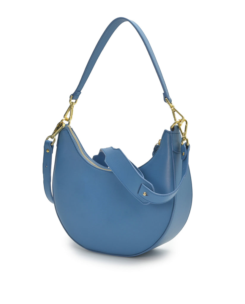 Imagen lateral asa doble de bolso media luna azul Leandra. Bolso de hombro multiposición con forma de media luna de piel color azul Leandra. Fabricado en UbrIque España