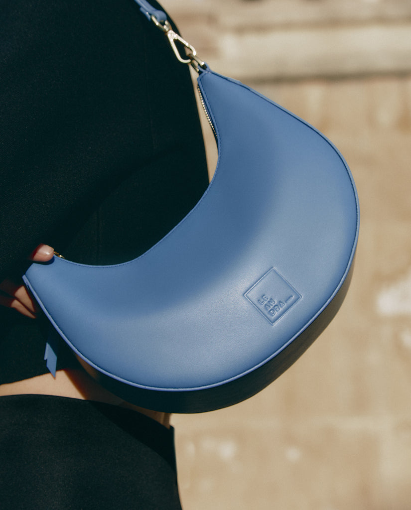 Bolso media luna de piel Leandra. Bolso de hombro multiposición con forma de media luna de piel color azul Leandra.