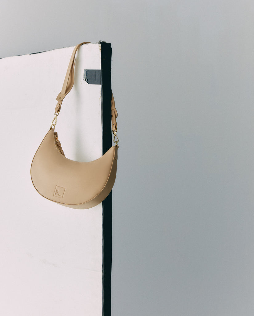 Bolso media luna beige. Bolso de hombro multiposición con forma de media luna de piel color beige Leandra. Made in Spain
