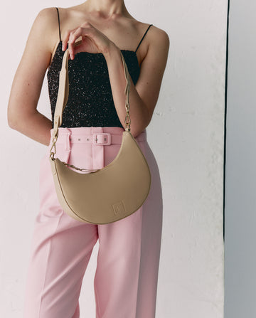 Imagen de modelo con bolso media luna beige. Bolso de hombro multiposición con forma de media luna de piel color beige Leandra.