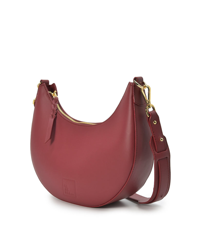 Imagen detalle cierre asa de bolso de hombro multiposición con forma de media luna de piel color burdeos Leandra.