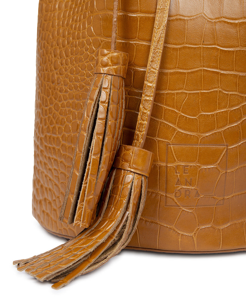 Bolso bucket bag grabado en coco color caramel Leandra. Bolsos fabricados en España Leandra. Imagen borlas bolso.
