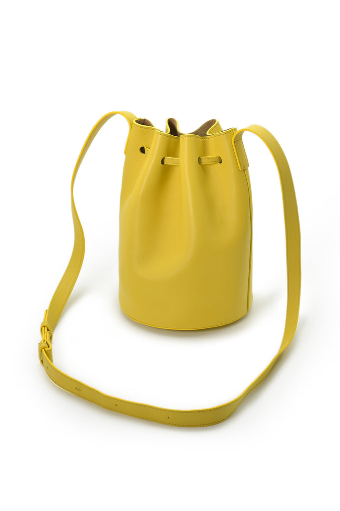 Mini bolso de piel tipo saco o Mini bucket bag color amarillo con bolsillo interior y borlas bicolor en nude Leandra. Made in Spain Leandra a la venta en leandrabrand.com Imagen detalle asas